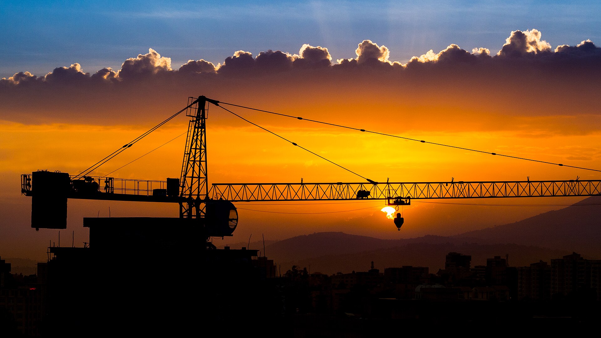Silhouette of a construction crane against an orange sunset over the Addis Ababa skyline