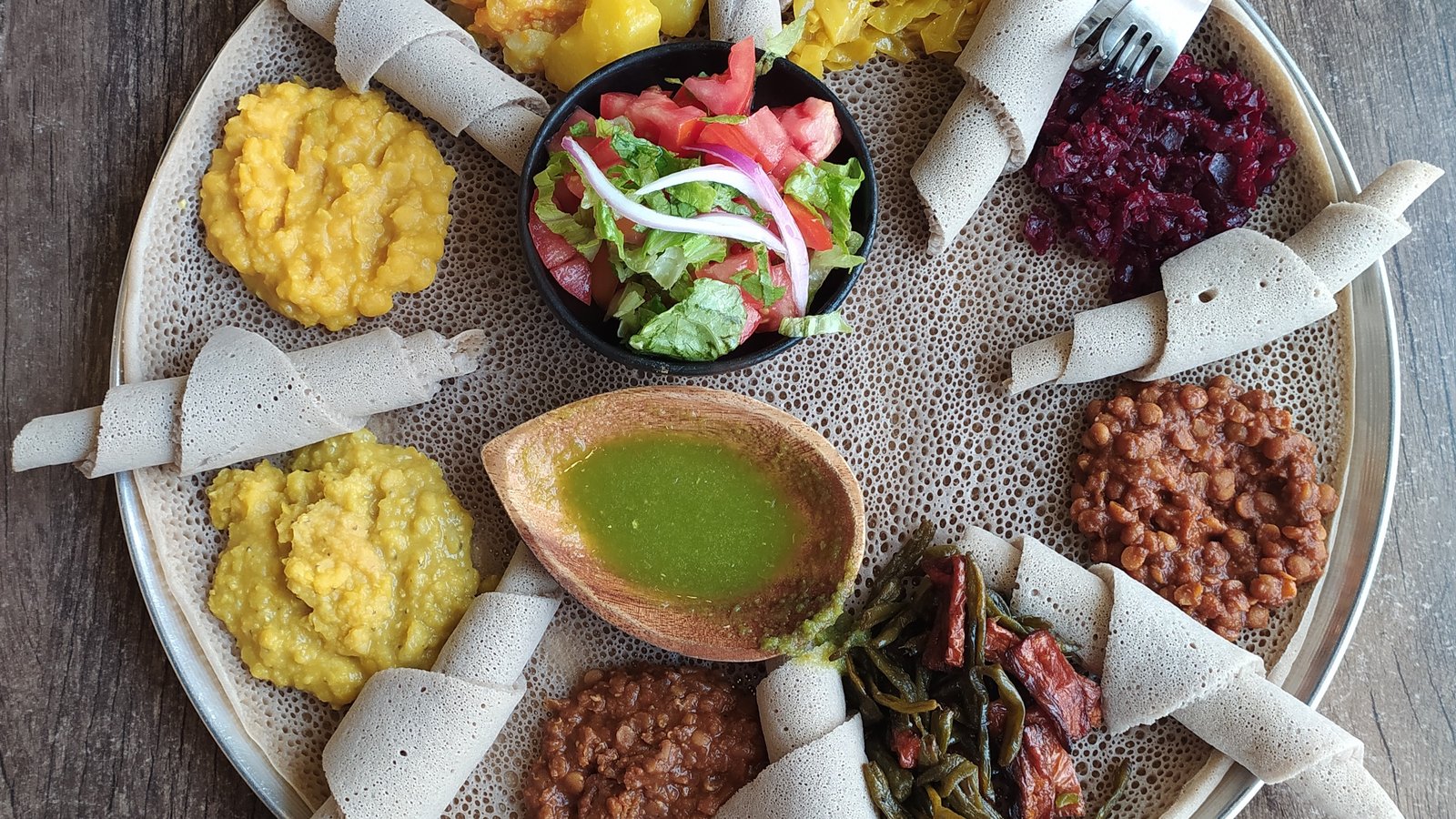 Injera topped with eight kinds of Ethiopian stews, with rolled injera around the plate